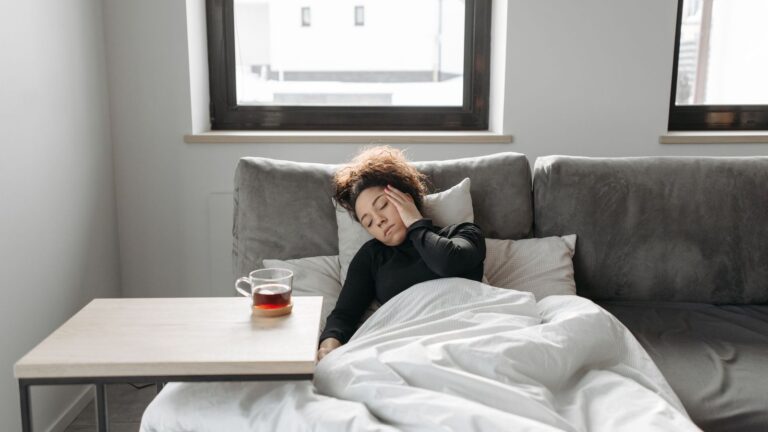 Person resting on a sofa with a warm drink while feeling unwell after a possible exposure