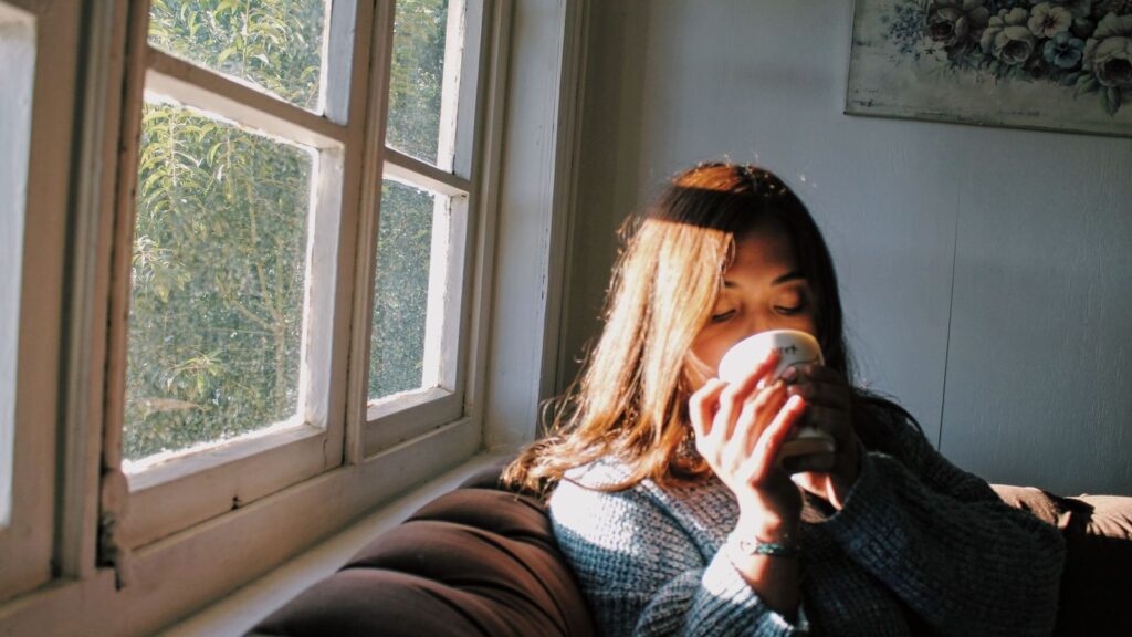 A person sitting calmly by a sunny window with a cup of tea, taking a quiet moment while waiting for test results