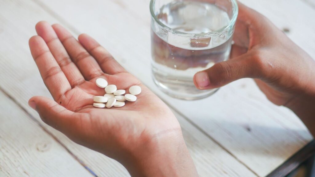 Two white tablets in an open palm with a glass of water, like the double first dose of on-demand PrEP