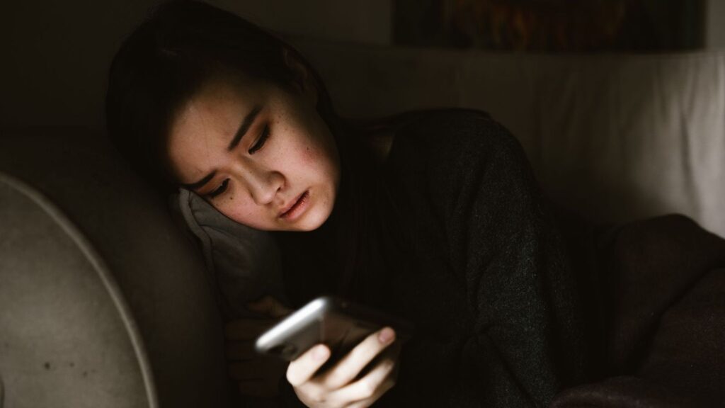 A worried person sitting on a bed at night, holding a phone and deciding who to call after a possible HIV exposure